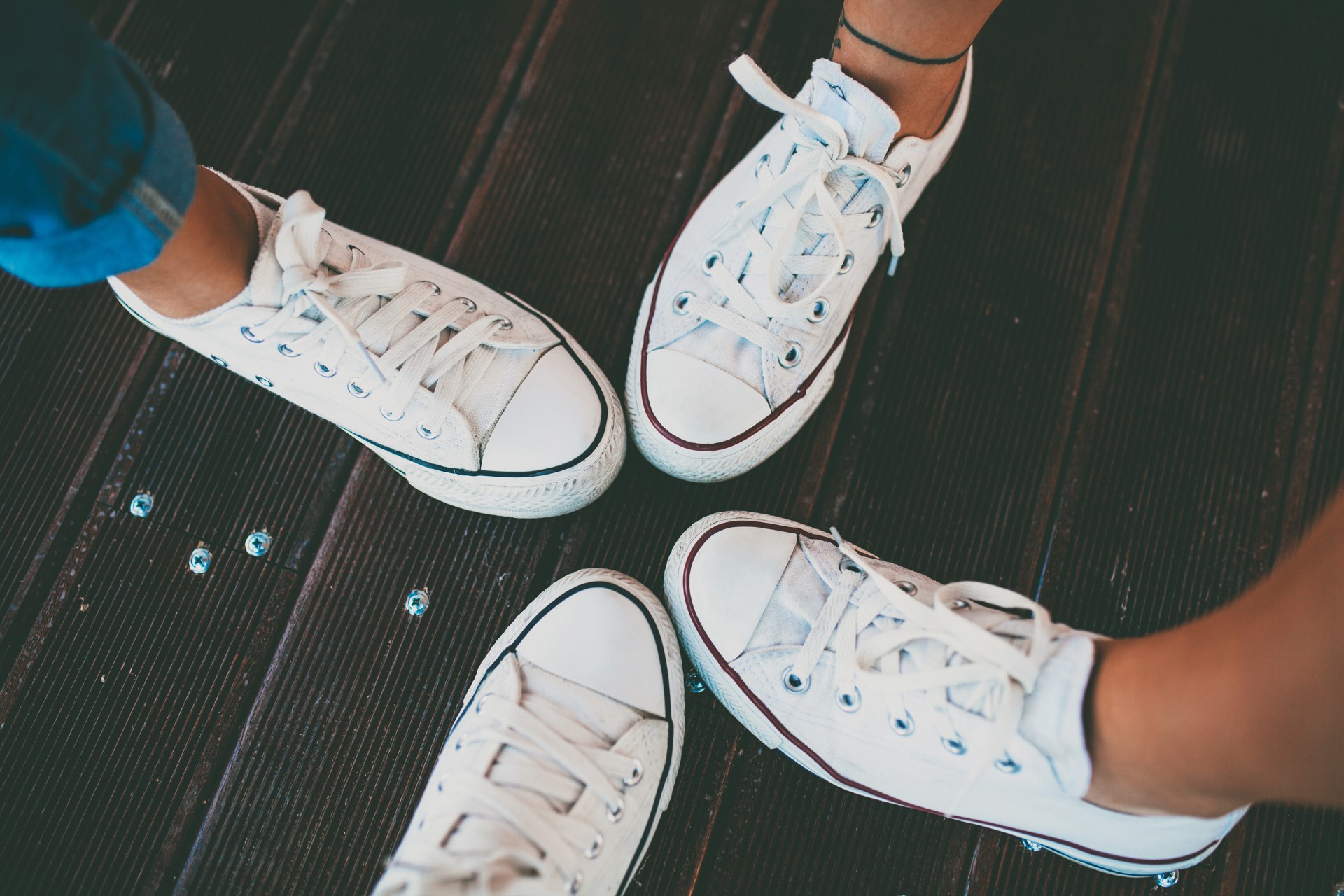 Closeup of hipster shoes. Best friends wearing same white footwear. White sneakers over wooden floor